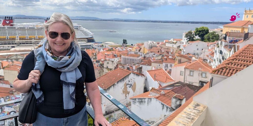 Woman smiling in sunglasses and scarf overlooking Lisbon rooftops, cruise ship in harbour, symbolising business breakthroughs and lifestyle freedom.