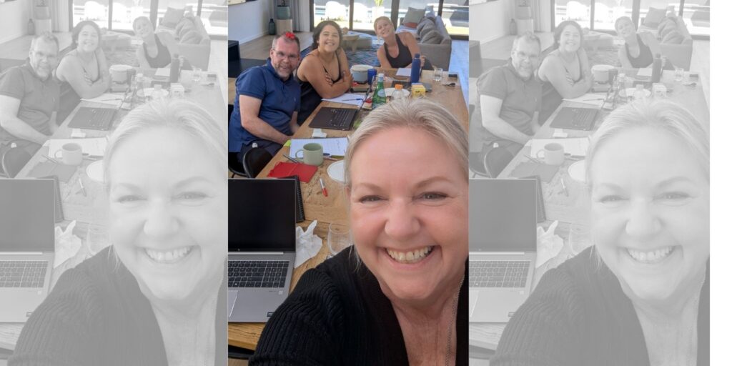 Mell Millgate smiling and taking a selfie during a relaxed business planning session with the RHM Law leadership team, seated around a table with laptops, notebooks and coffee.